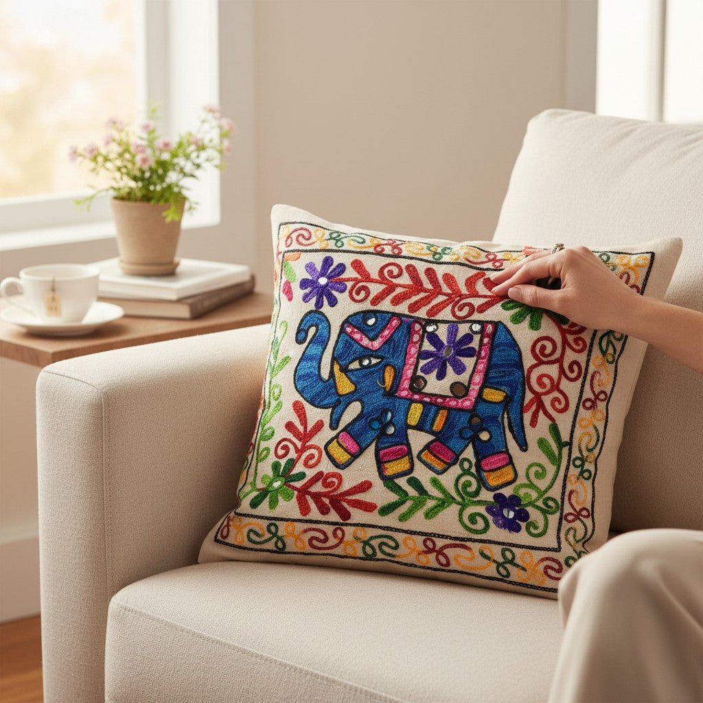 Cream cushion cover with a blue elephant and colorful floral motifs displayed on a white armchair.